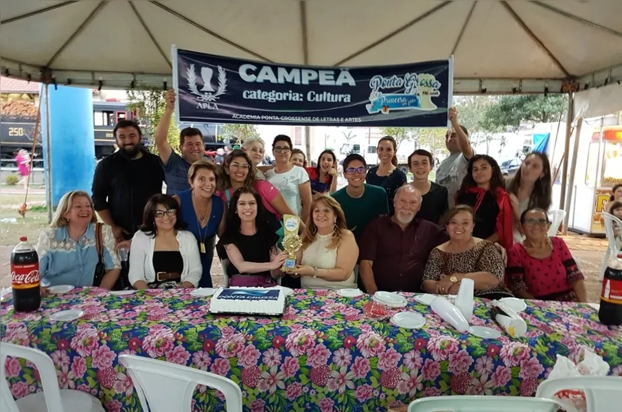 A Academia Ponta-grossense de Letras e Artes (APLA) em momento descontraído de comemoração, entre integrantes e amigos, da vitória na categoria Cultura na gincana “Princesa em Festa”, promovida pela Prefeitura Municipal de Ponta Grossa. A entidade realizou a tarefa de vinte dias de intervenções poéticas pela cidade, da lista de 196 presentes para a cidade por seu aniversário. Na foto com a vice-prefeita Elizabeth Schimdt. O mérito é resultado do empenho de todos e, principalmente, da presidente, Dione Navarro.